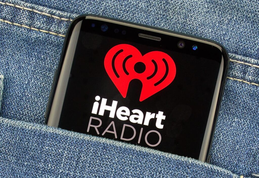 Close up of a smartphone screen in a pocket with the iHeartRadio logo displayed on the screen.
