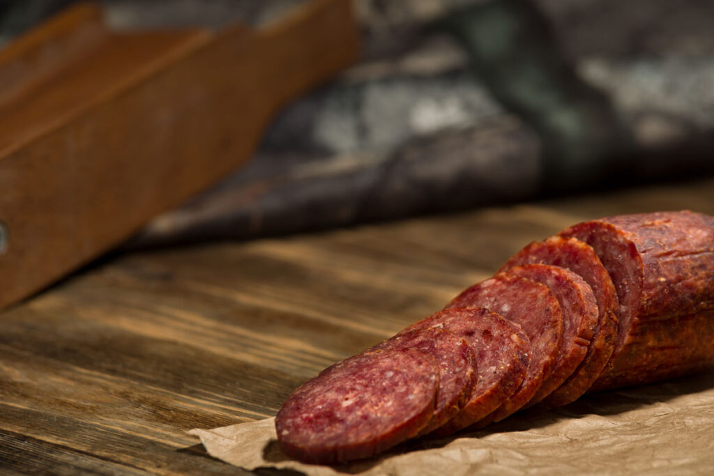 Close up of sliced sausage on a wood cutting board.