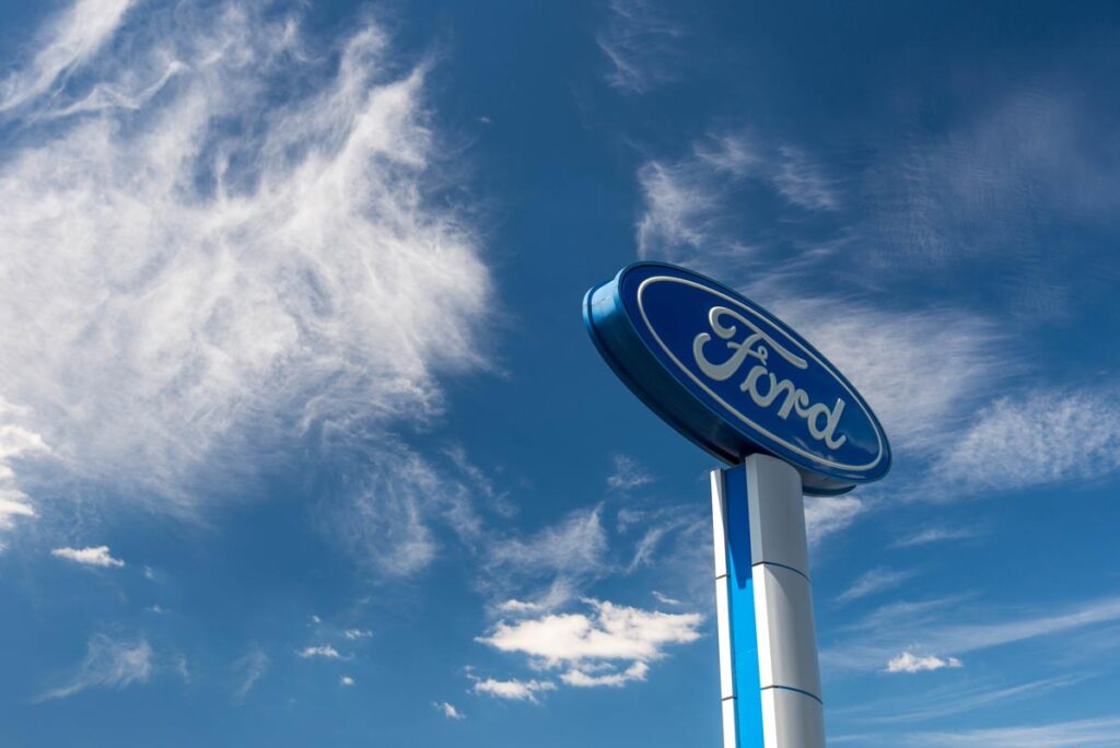 Ford logo against blue sky with white clouds.