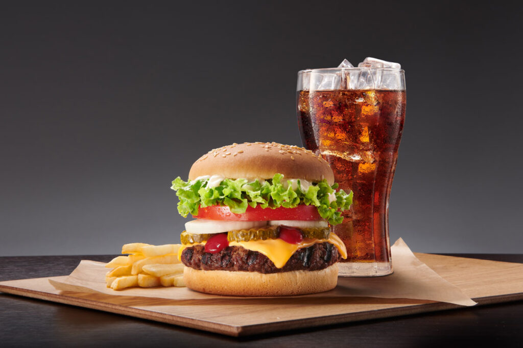 Burger, fries, and coke on a wooden board against a gray backdrop.