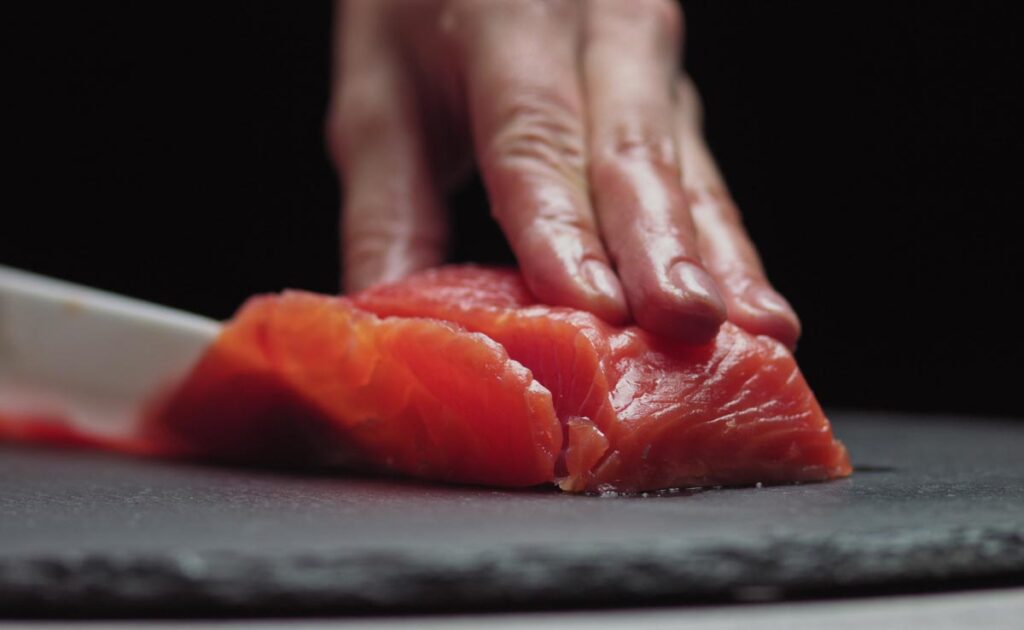 Close up of a chefs hands cutting salmon, representing the salmon price-fixing class action settlement.