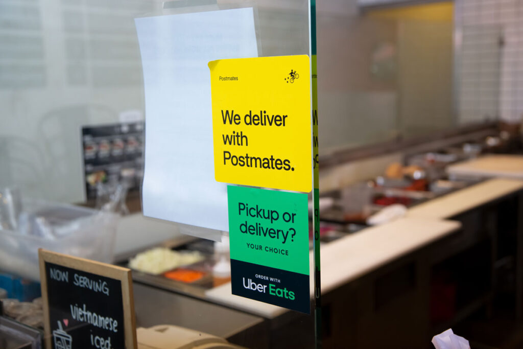A view of window stickers advertising the availability of food delivery service through Postmates and Uber Eats.