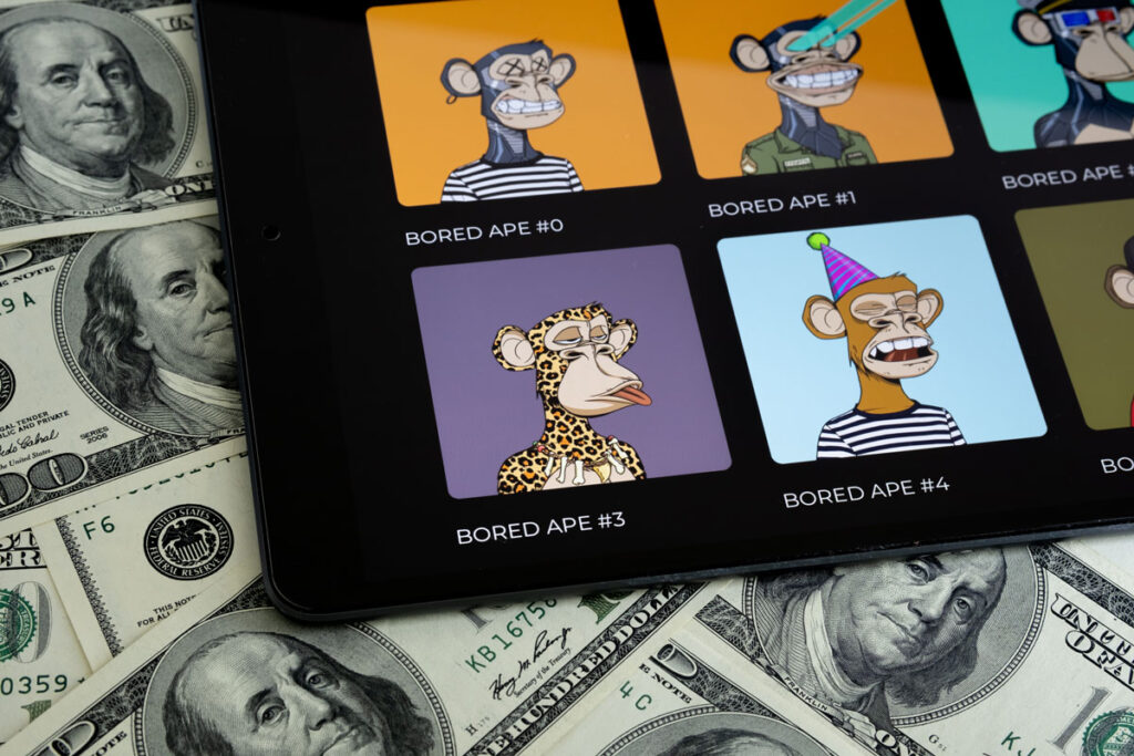 Colección de arte digital BORED APE NFT vista en la pantalla de una tableta colocada sobre billetes de 100 dólares.