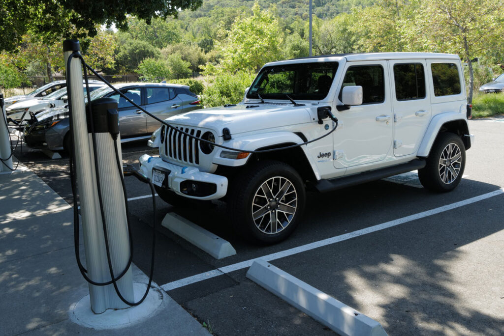 A 2022 Jeep Wrangler 4xe electric vehicle is parked while being charged with others at a solar powered EV charging station.