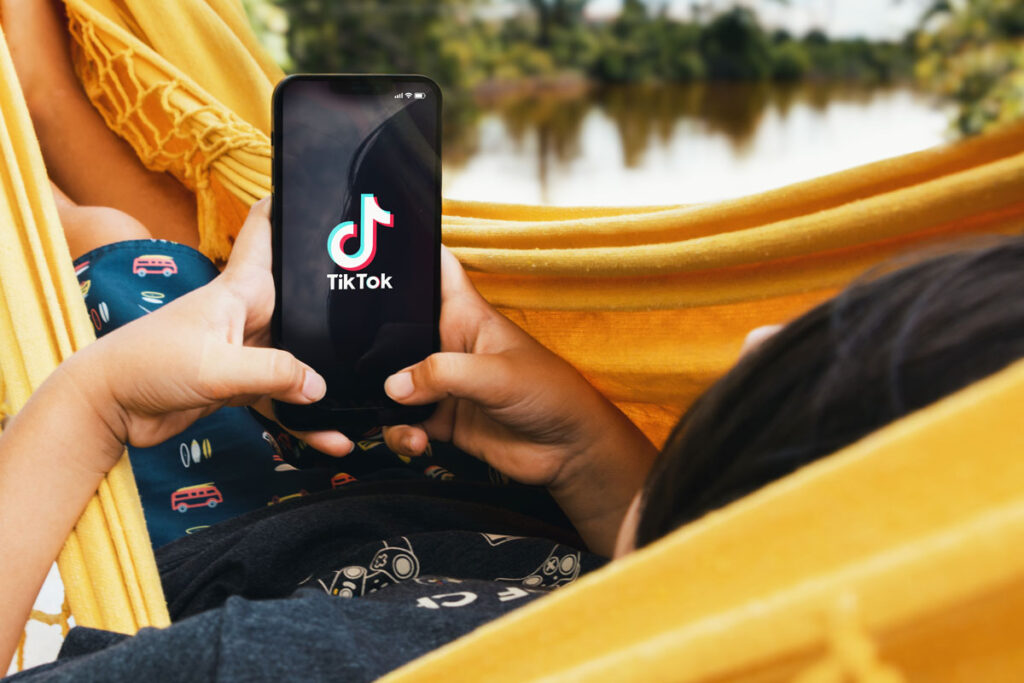 Child lying in hammock with Tik Tok app on smartphone screen.