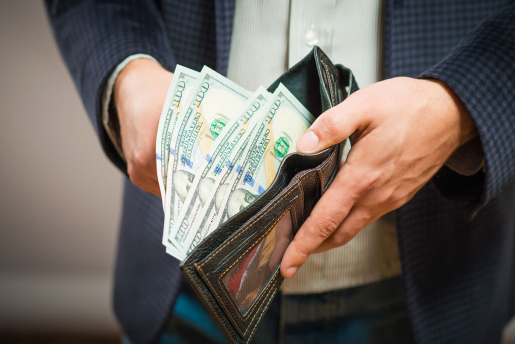 Close up of a businessman's hands holding a wallet containing hundred dollar bills, representing the Federal Trade Commission (FTC) refunds.