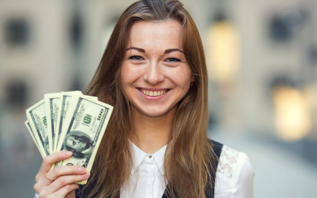 Young woman smiling holding US currency.