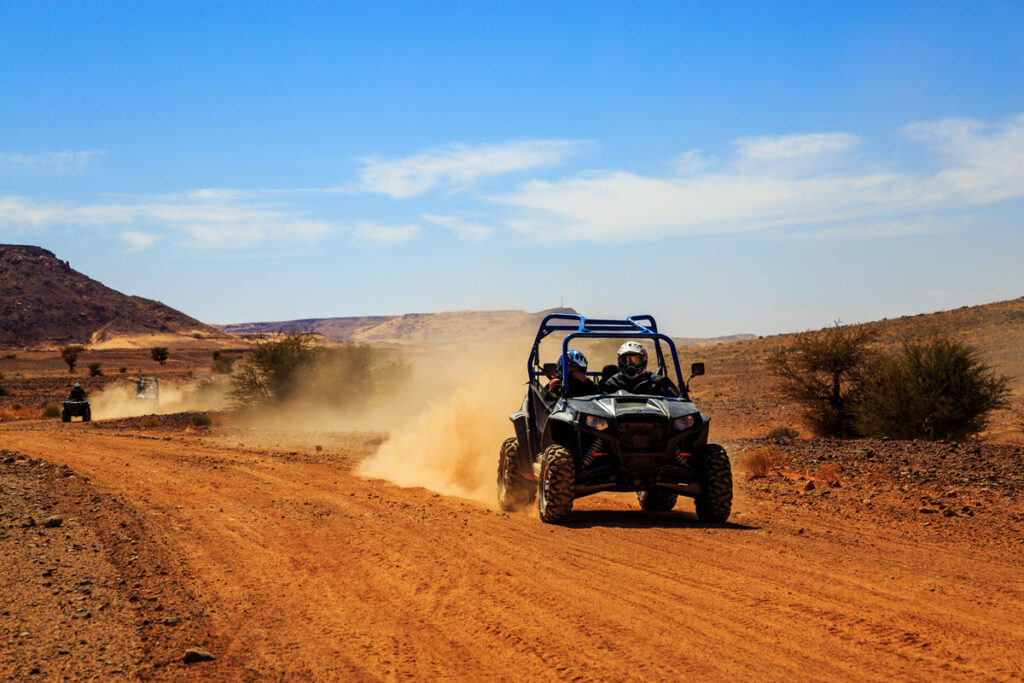 An offroad vehicle driving in the desert against a bright blue sky.