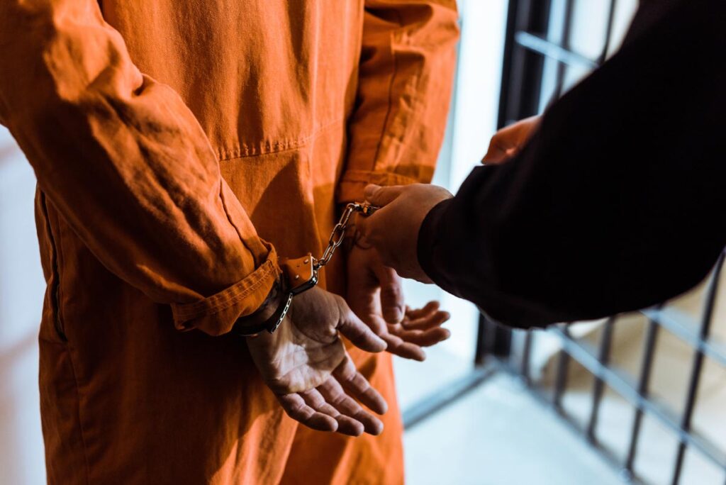 A close-up of an officer putting handcuffs on a prisoner, representing the New York City bail over-detention class action lawsuit settlement.