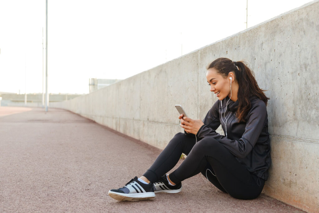 A young athletic woman sitting on track while looking at her smartphone, representing The Athletic automatic renewal class action