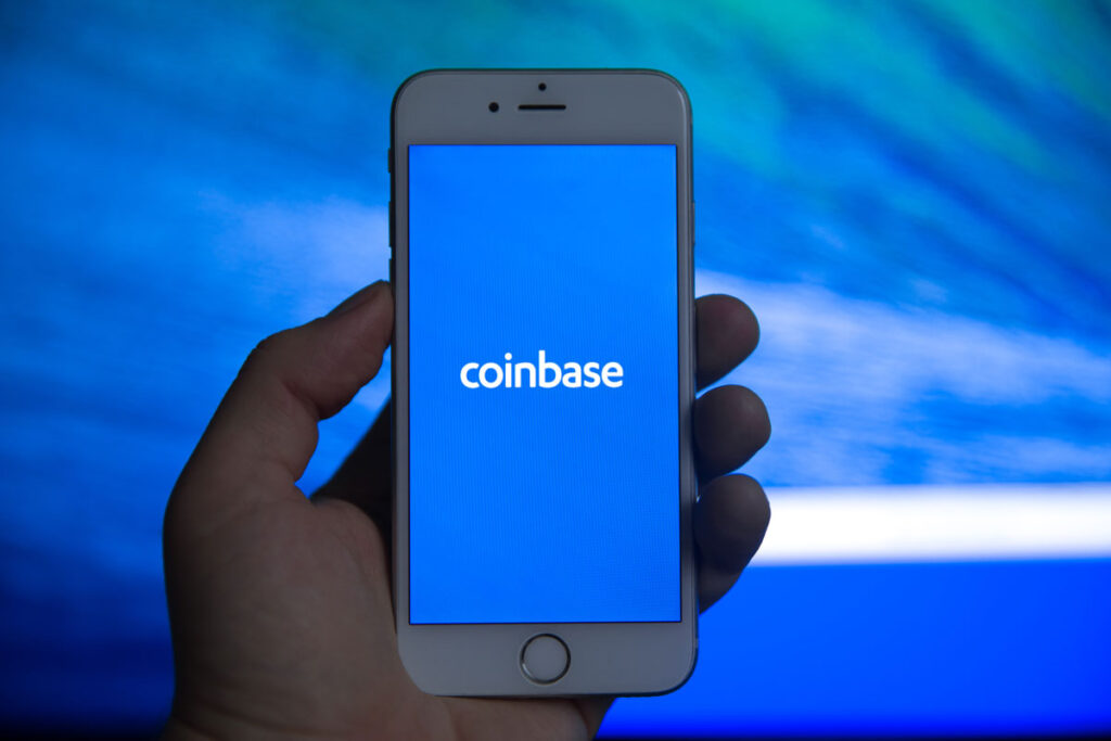 Hand holding a smartphone with Coinbase logo displayed.