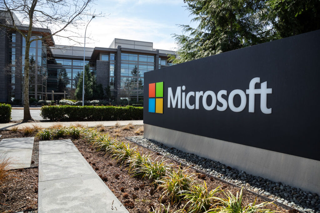 Wide angle view of a Microsoft sign at the headquarters for the software and hardware company, with office building in the background.