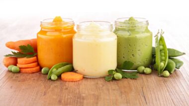 ready-made baby food in jars surrounded by vegetables, on a wooden table.
