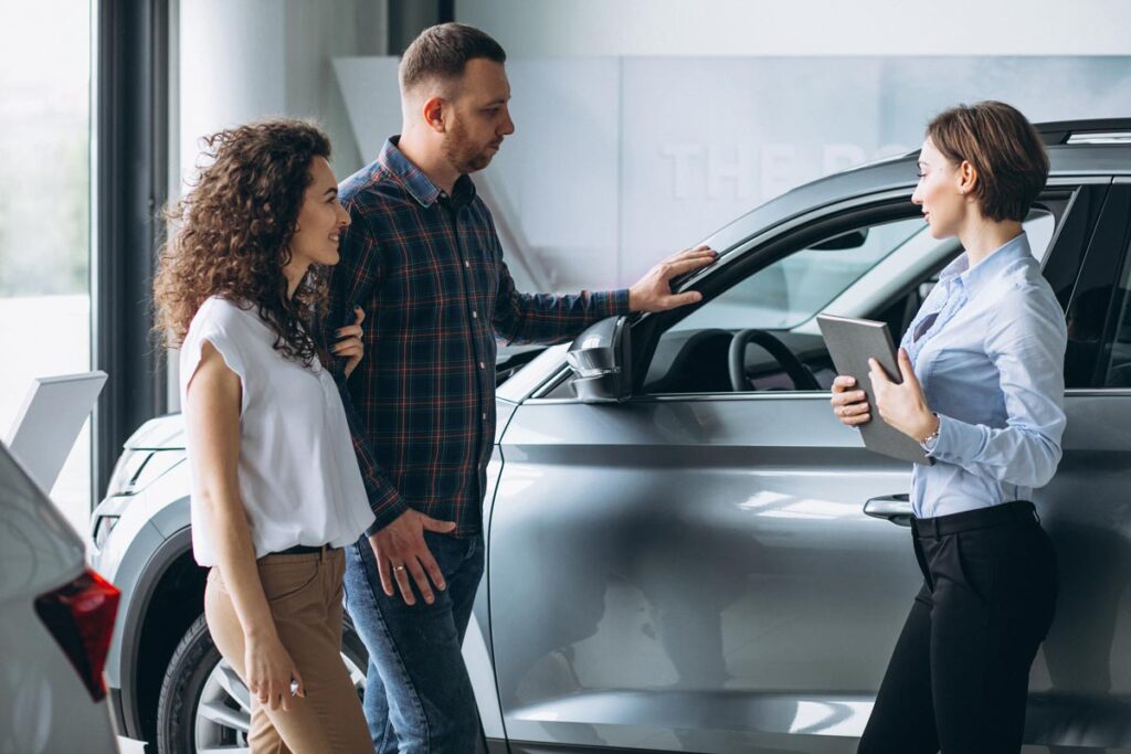 Young couple talking to a sales person in a car showroom, representing the Volkswagen and Audi data breach class action lawsuit settlement.