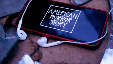 Headphones and Iphone 11 pro with the American Horror Story logo.