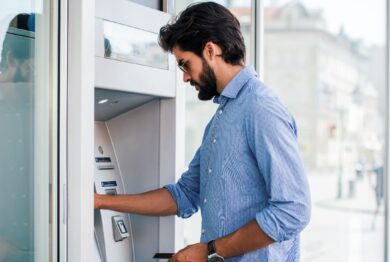 Man depositing money at automatic teller machine, representing the returned deposit bank fees investigation.