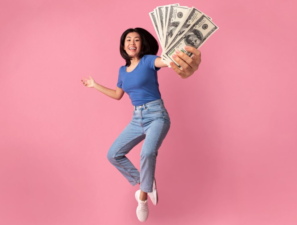 Happy women jumping for joy with money in hand, representing class action settlement payments.
