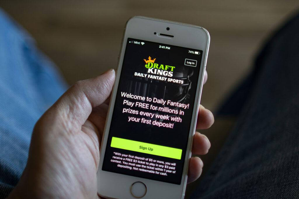 Close up of a hand holding a smartphone with the Draft Kings website displayed.