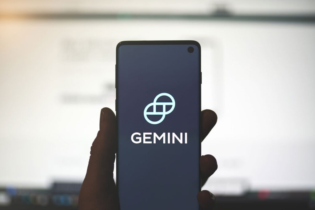 Man holding a smartphone with Gemini app logo with blurred website background.
