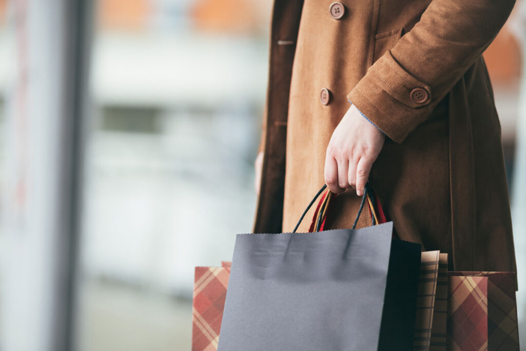 Elegant and modern woman in brown leather jacket or topcoat standing on the city street and holding bunch of shopping bags.