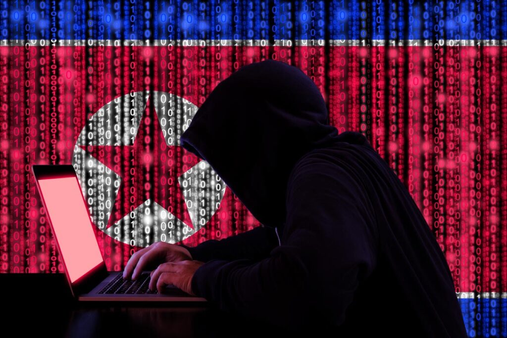 디지털 북한 국기와 바이너리 스트림 배경이 있는 노트북 앞에 앉아 있는 어두운 후드를 쓴 해커.