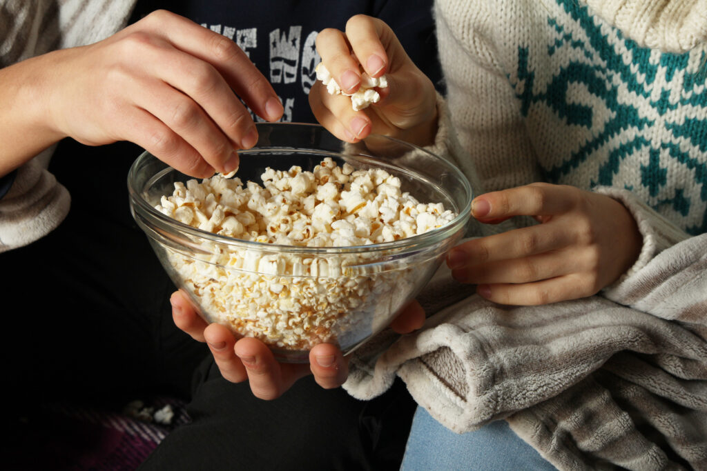 Young people watch movies and eating popcorn with a glass bowl, close-up.