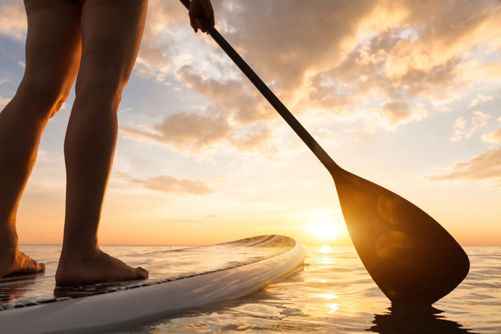 Close up of a person on a stand up paddle boarding on a quiet sea with warm summer sunset colors.