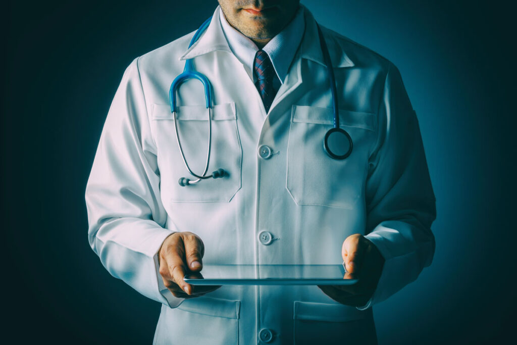 Doctor in a white labcoat and stethoscope holding a tablet, representing the Logan Health data breach class action lawsuit settlement.