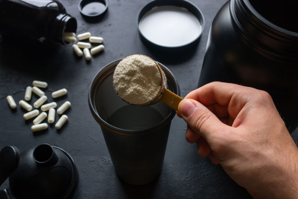 Close up of an athletes hands making a protein powder drink with supplements in the background.