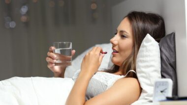 A girl in bed taking a pill.