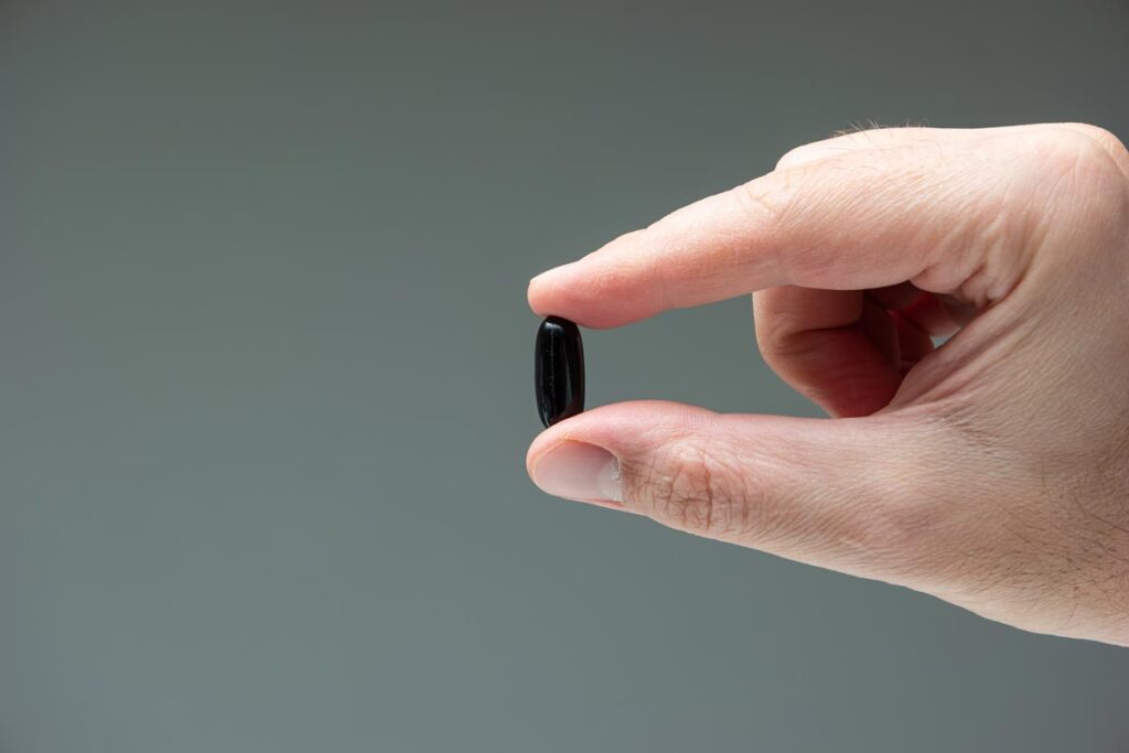 Caucasian male hand holding a black medicine capsule pill between fingers close up, representing the Volt Candy  PrimeZen Black 6000 erectile disfunction pill recall
