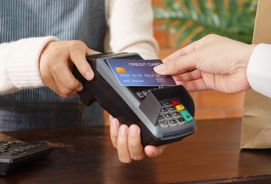 Close up of a hand paying with a credit card on a POS system, representing the proposed CFPB credit card late fees rule.