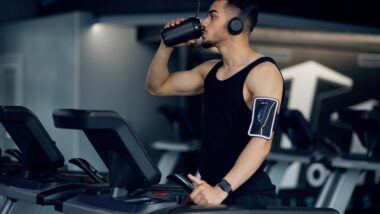 Muscular Arab Guy Drinking Protein Cocktail From Sport Shaker While Training On Treadmill At Gym.