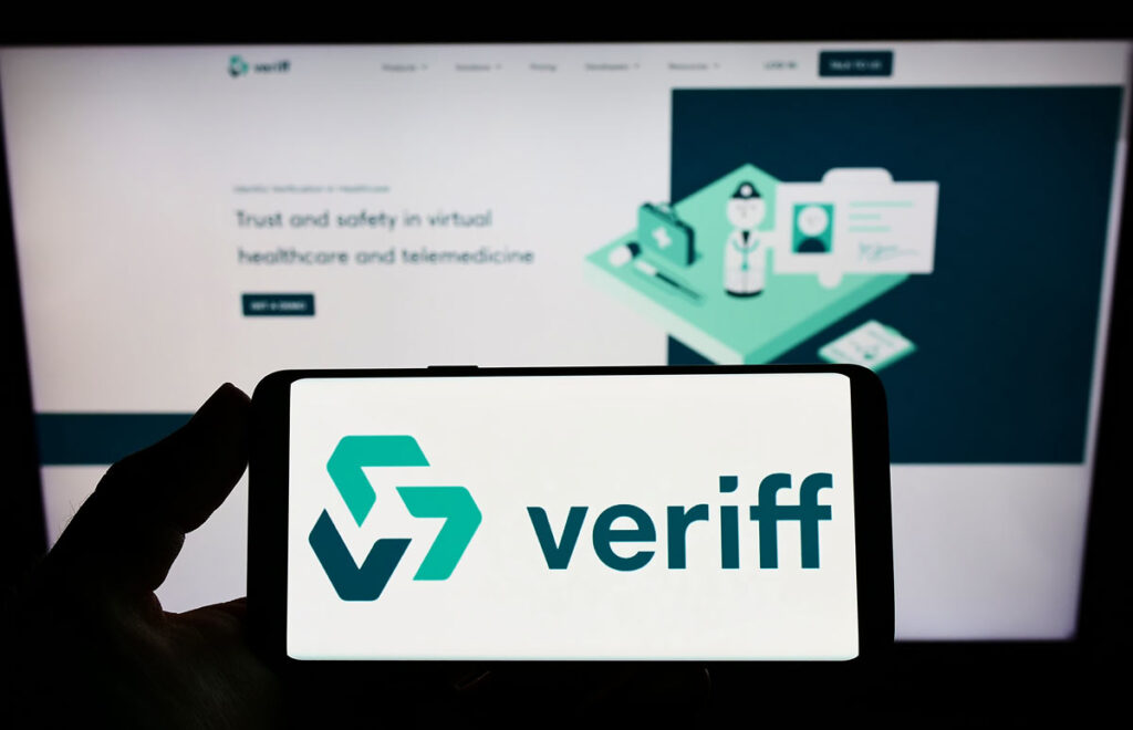 Person holding smartphone with logo of Estonian identity verification company Veriff on screen in front of website, representing the Veriff BIPA class action settlement.
