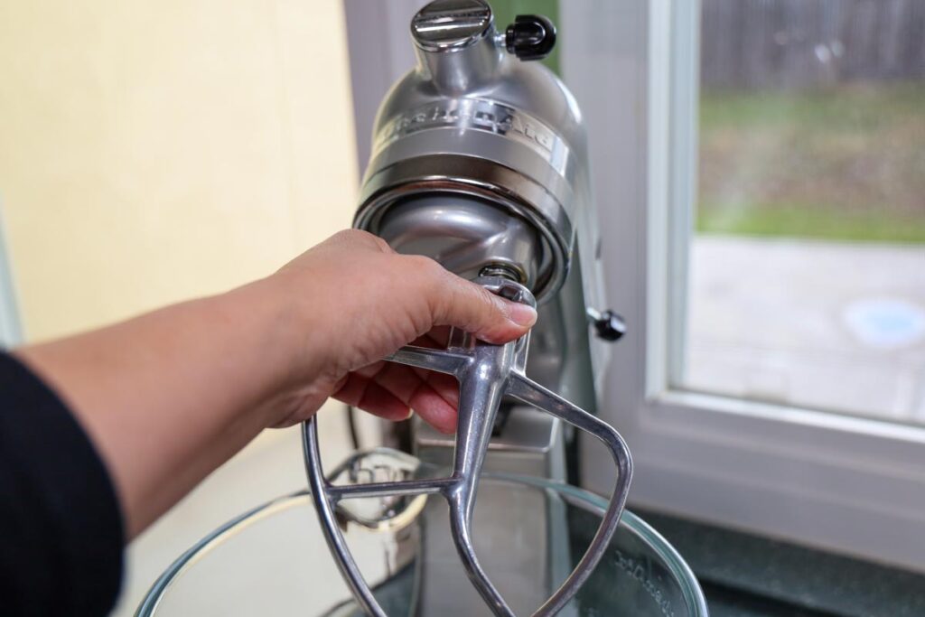 View of a female's hand putting a paddle attachment on a Kitchenaid stand mixer, representing the "fake" mixer recall.