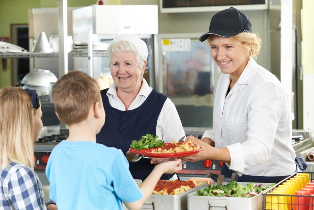 Lunch ladies serving students in a cafeteria, representing USDA nutrition guidelines