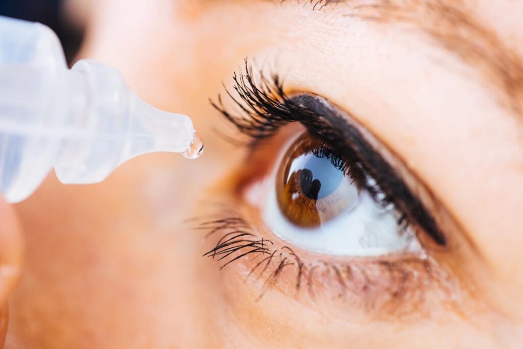 Close up of a woman putting eye drops in her eye, representing the Ezricare eye drop bacteria class action.