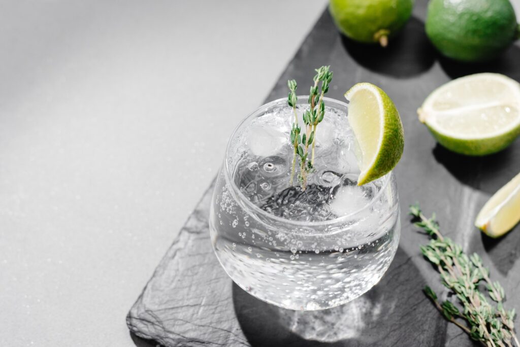 A sparkling beverage is seen in a clear glass surrounded by limes and herbs, representing the Vizzy class action lawsuit settlement.