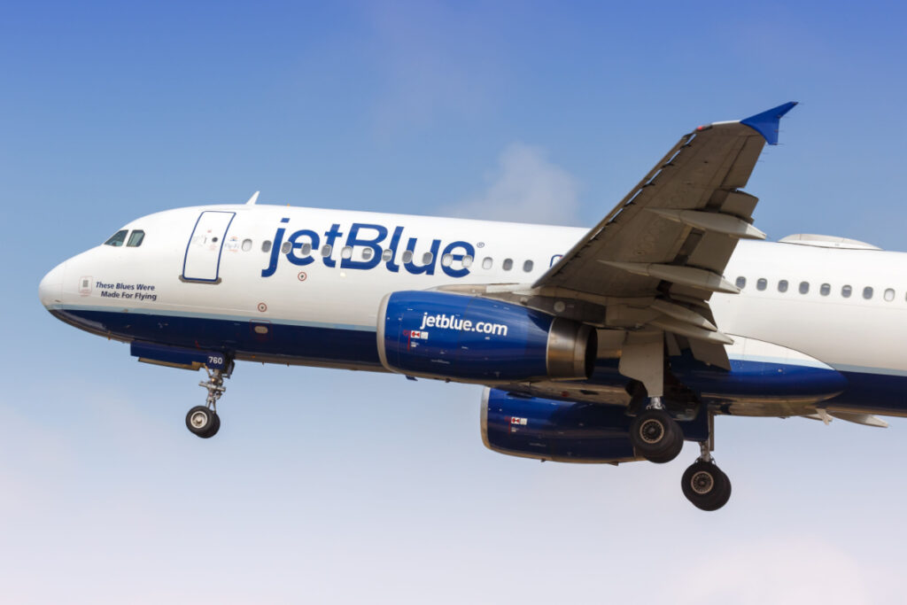 A JetBlue plane flies, representing the JetBlue and Spirit merger.