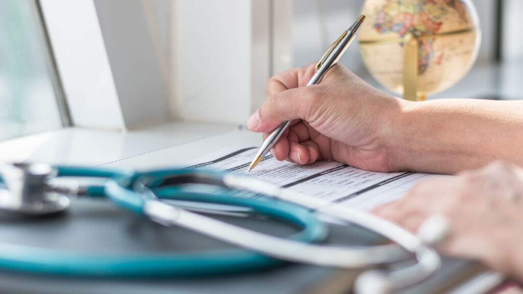 Doctor writing on paper near a stethoscope representing the Orlando Family Physicians data breach class action settlement.