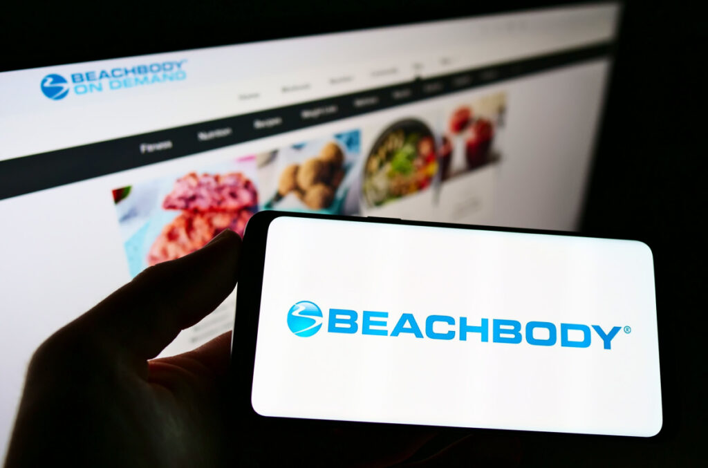 Person holding cellphone with logo of US fitness and media company Beachbody LLC on screen in front of business webpage.