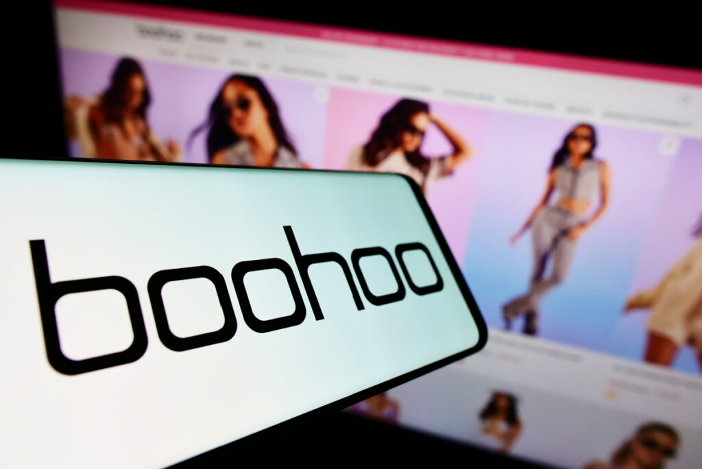 Cellphone with logo of British fashion company Boohoo Group plc on screen in front of business website.