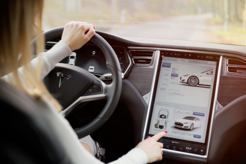 The interior of a Tesla Model S electric vehicle with woman driving and touching its large touchscreen dashboard, representing the Tesla camera recordings report