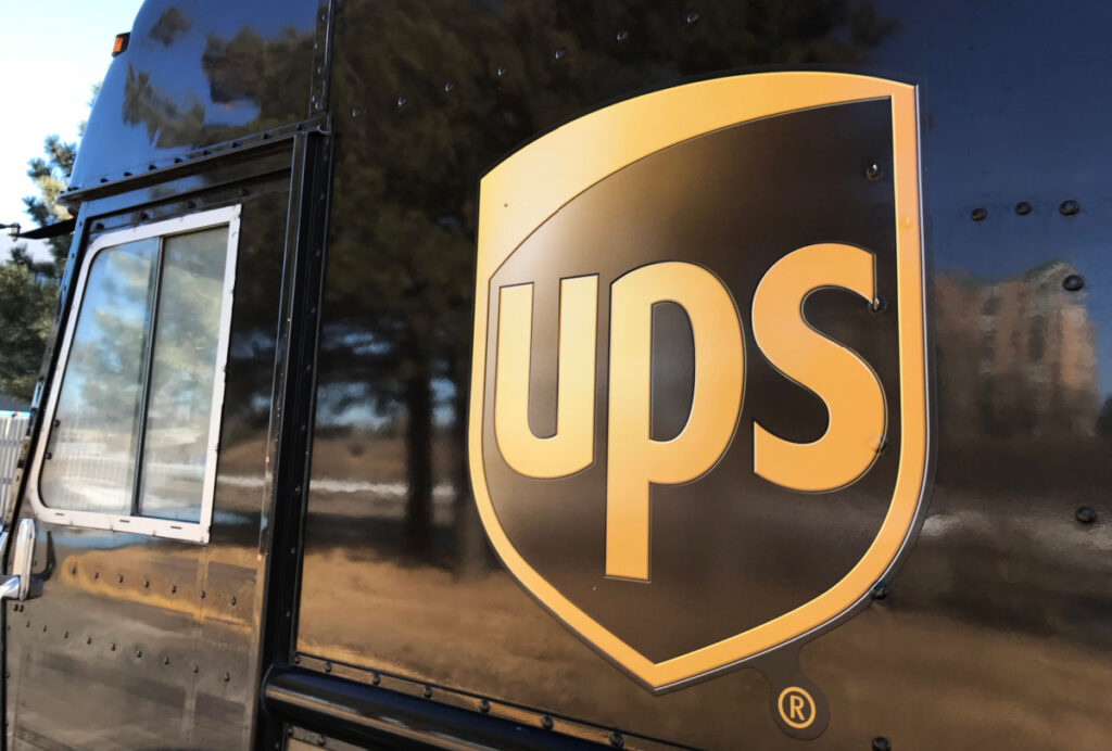 The side of a UPS delivery truck parked at a building as the driver makes deliveries, representing the UPS military leave class action lawsuit.