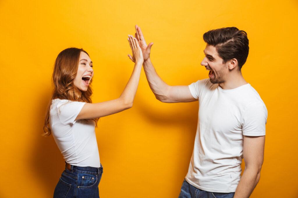 A woman and man giving each other a high five in front of a yellow background