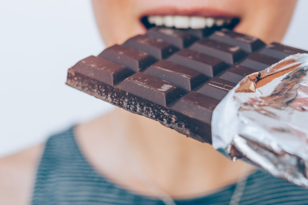 A woman biting into a dark chocolate bar