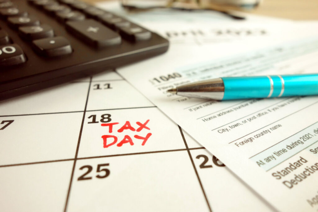 Tax Day written on a desk calendar w/ calculator & pen