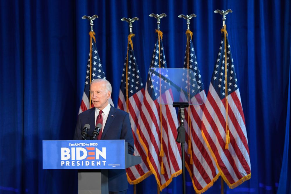 Democratic President Joe Biden stands behind a podium in front of five flags, representing the proposed transgender student-athletes rule