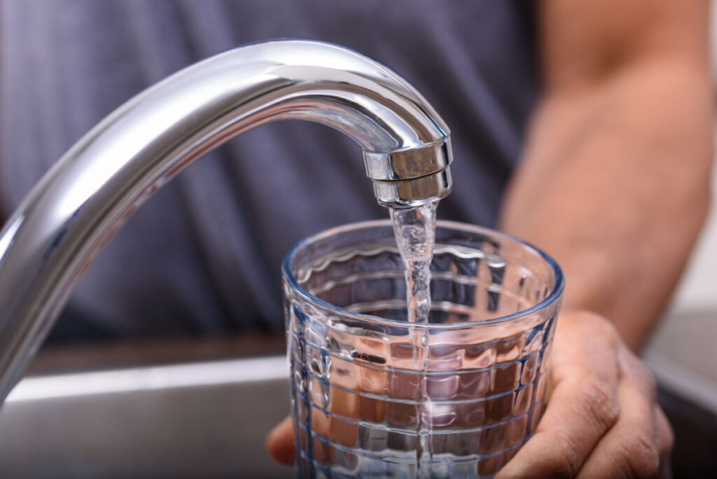 Man hand with a drinking glass filling potable water from kitchen faucet