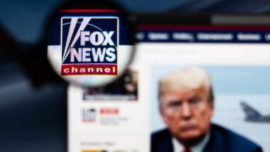 Fox News website homepage. Fox News channel logo visible through a magnifying glass.